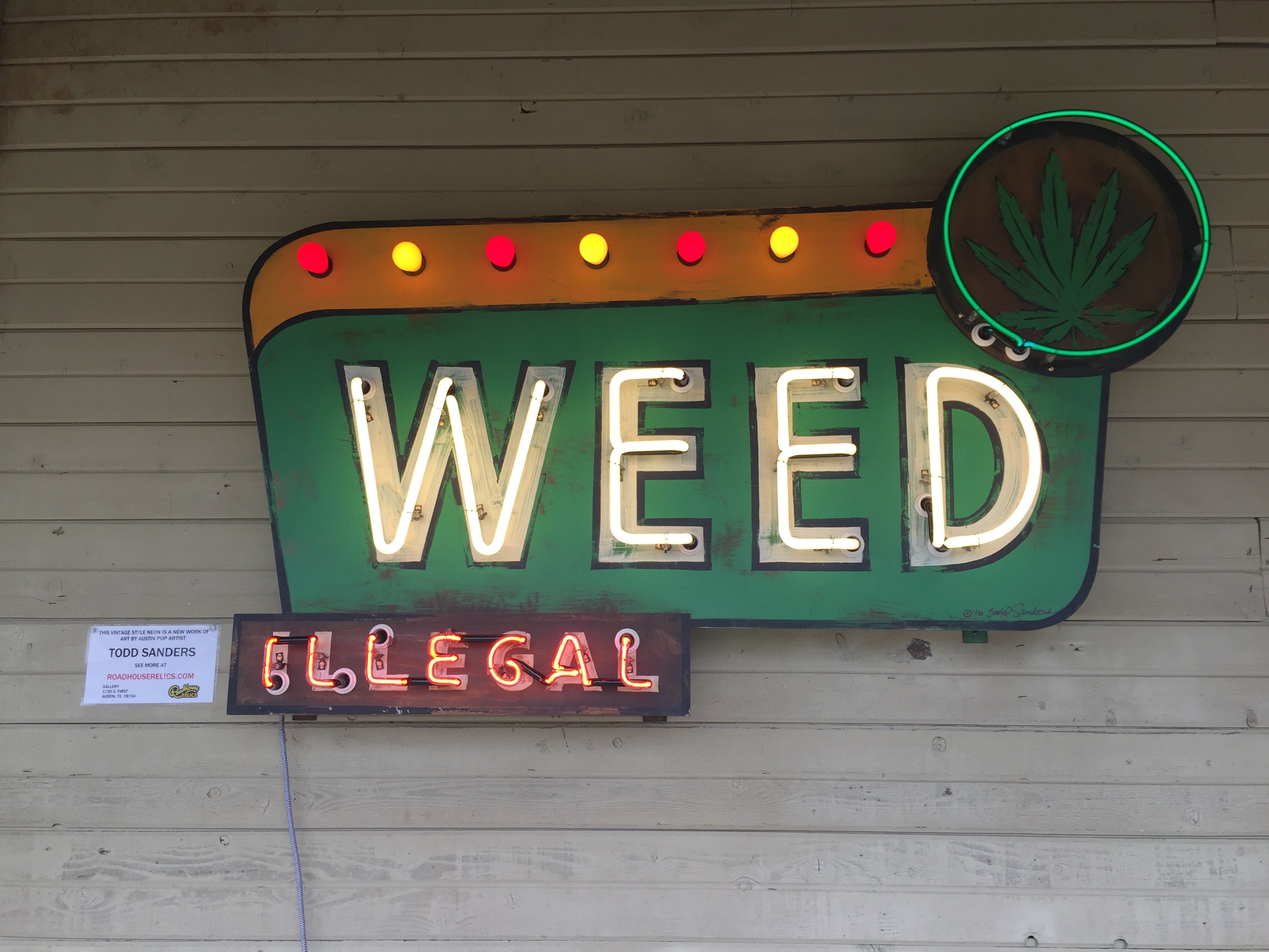 Neon sign with 'WEED' and 'ILLEGAL' text on a wooden wall