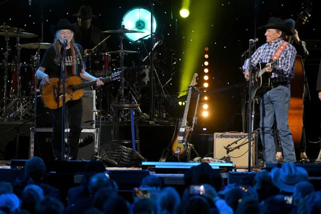 Willie Nelson and George Strait on stage with instruments and a crowd in front