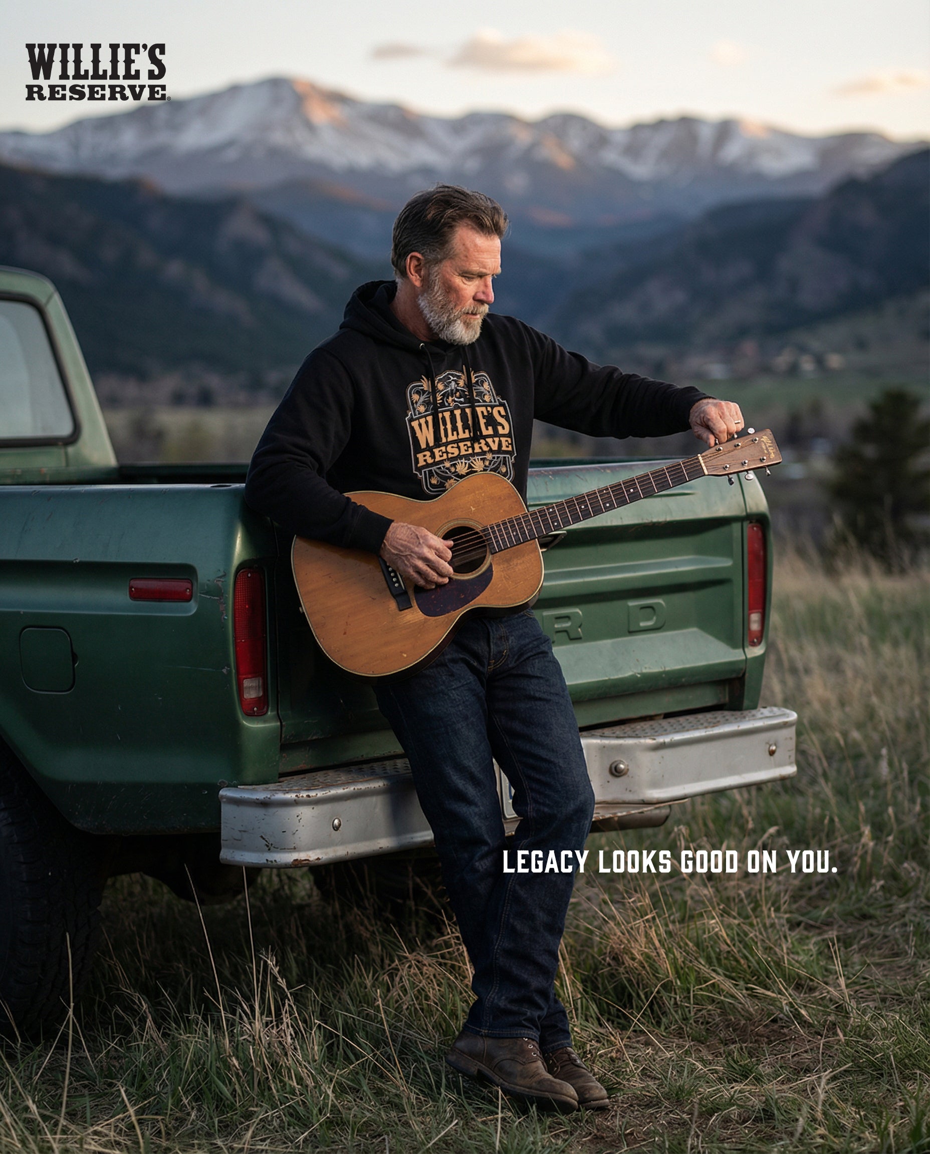 Man playing guitar in the back of a green truck with mountains in the background, featuring Willie's Reserve branding.