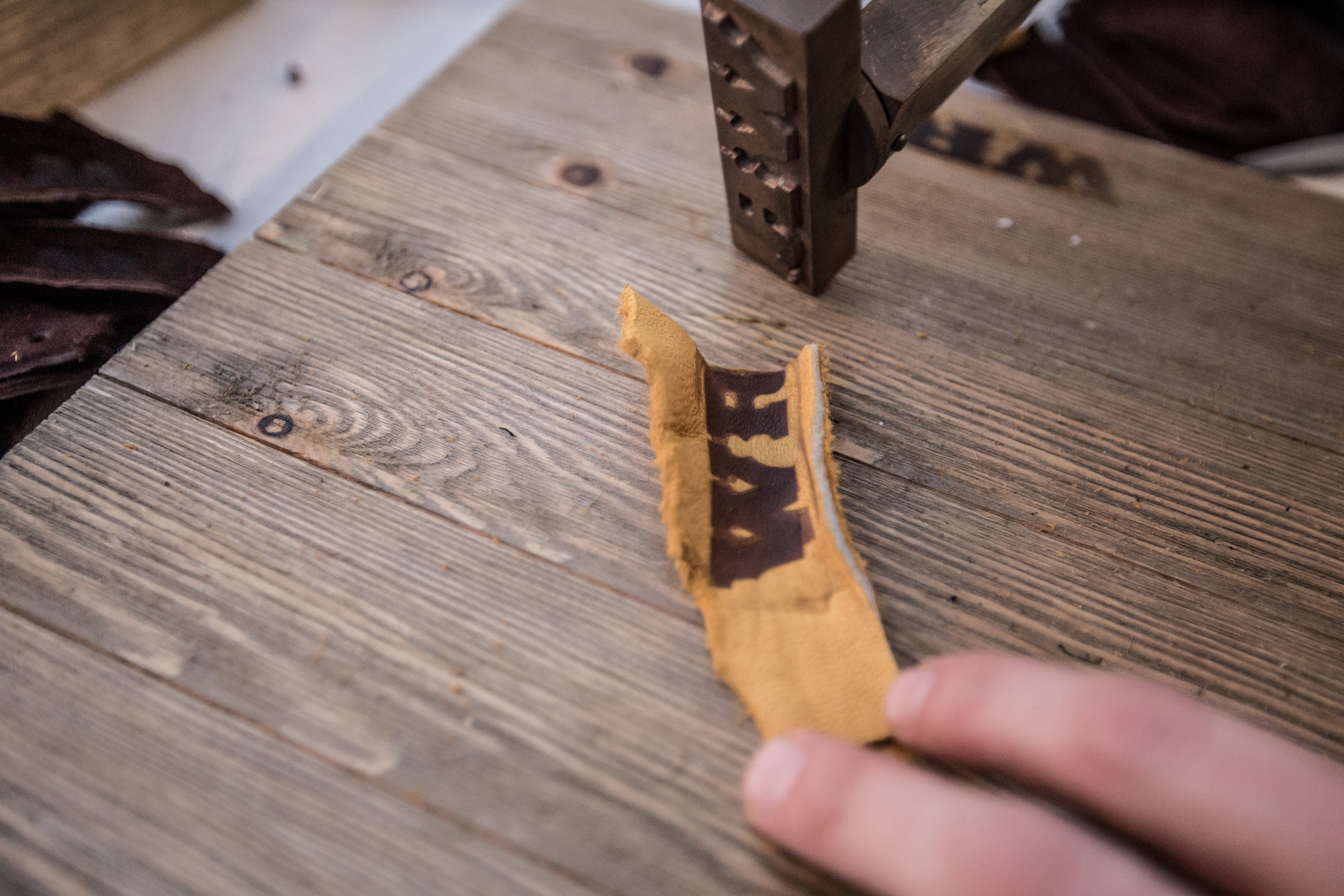 Hand holding a piece of leather with branding on a wooden surface
