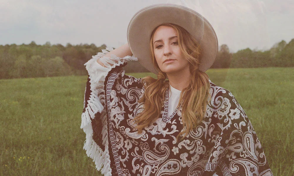 Woman in a patterned poncho and hat standing in a field