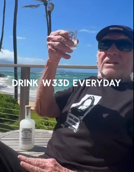 Willie Nelson holding a glass with text 'DRINK W33D EVERYDAY' by the ocean.