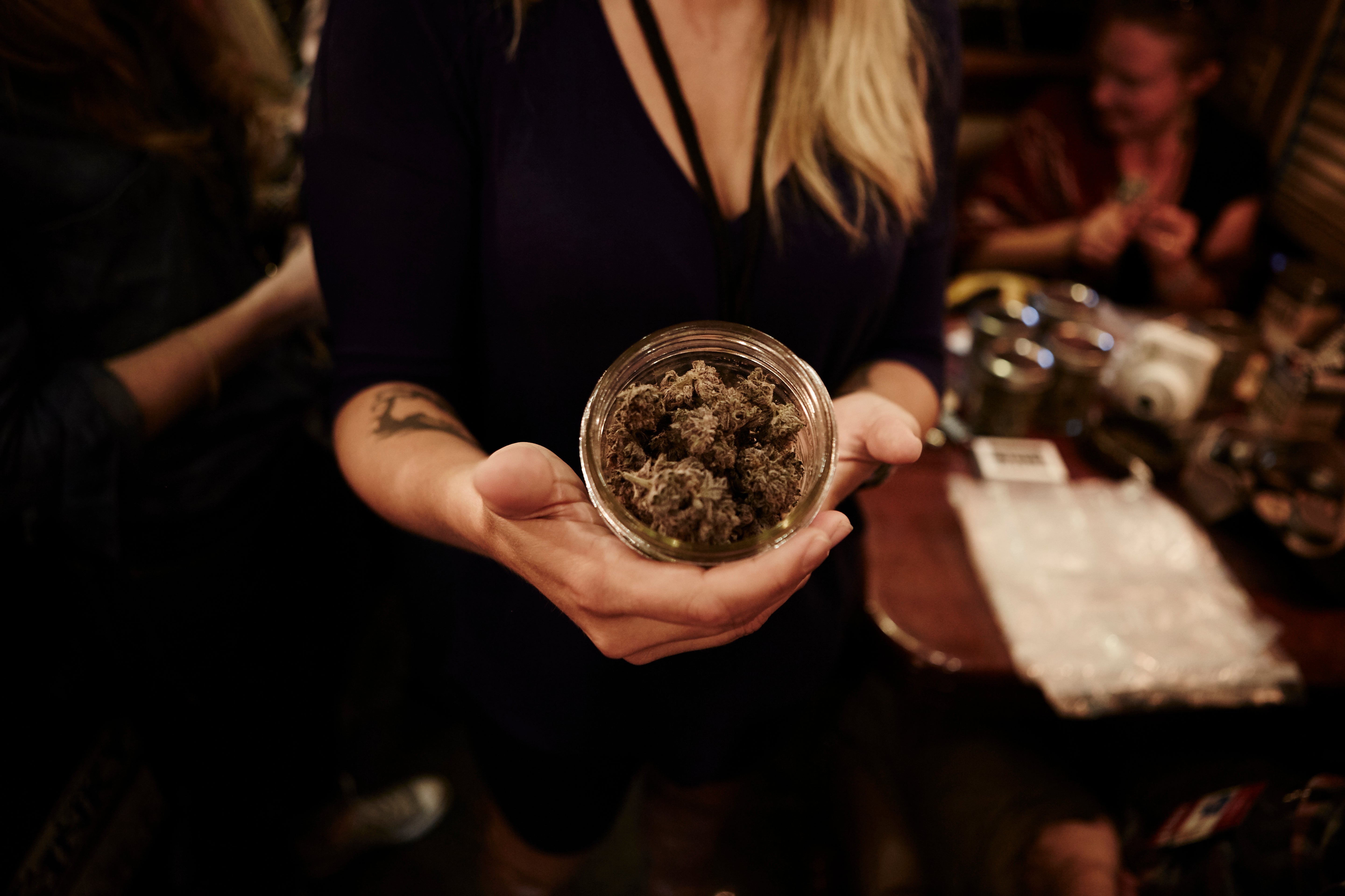 Person holding a jar of cannabis buds in a dimly lit indoor setting.